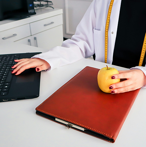 Ärztin tippt mit einer Hand auf der Tastatur und hält in der anderen ein Apfel